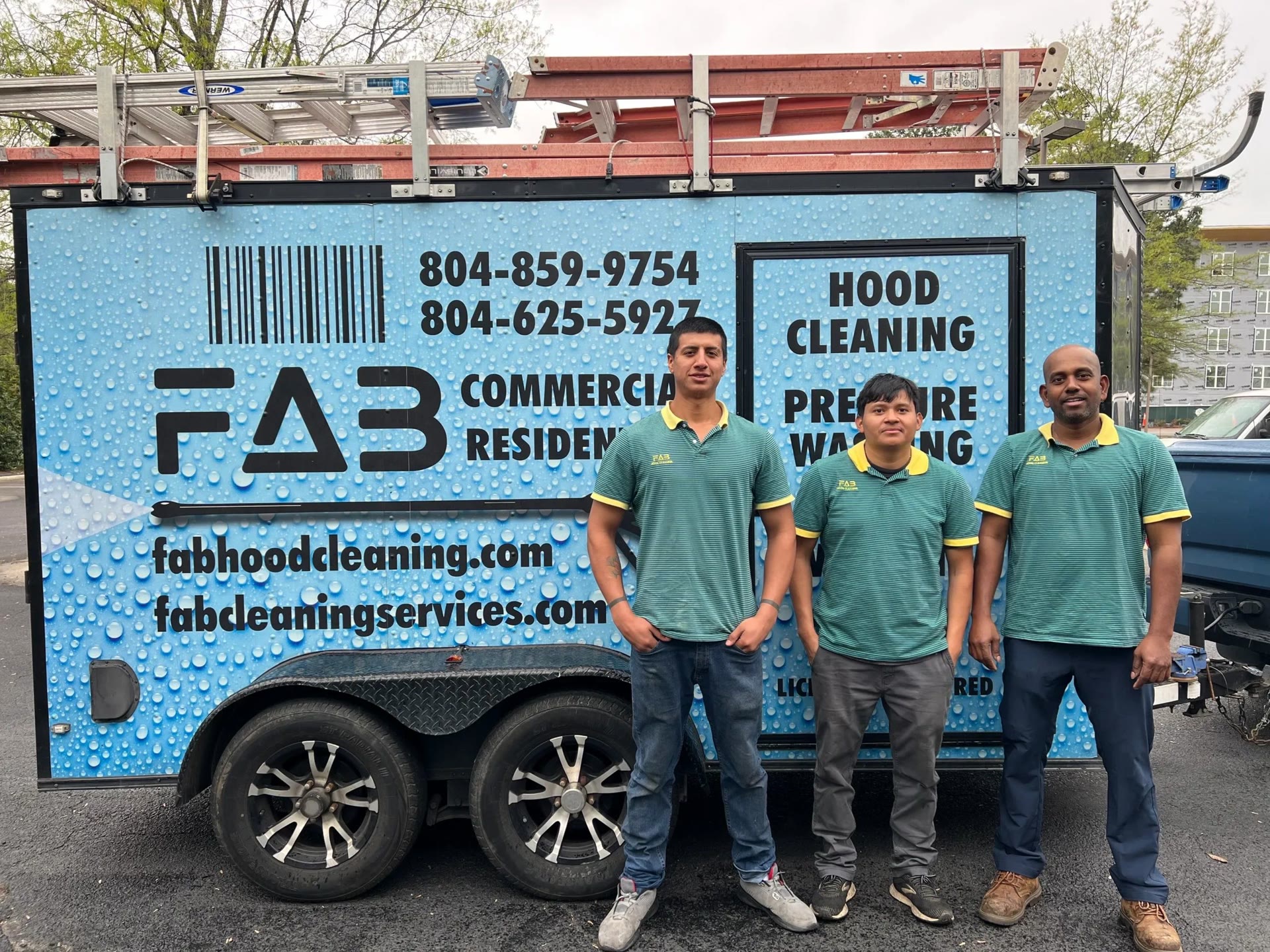 Three Fab Hood Cleaning technicians in green and yellow polo shirts in front of the company's blue branded trailer
