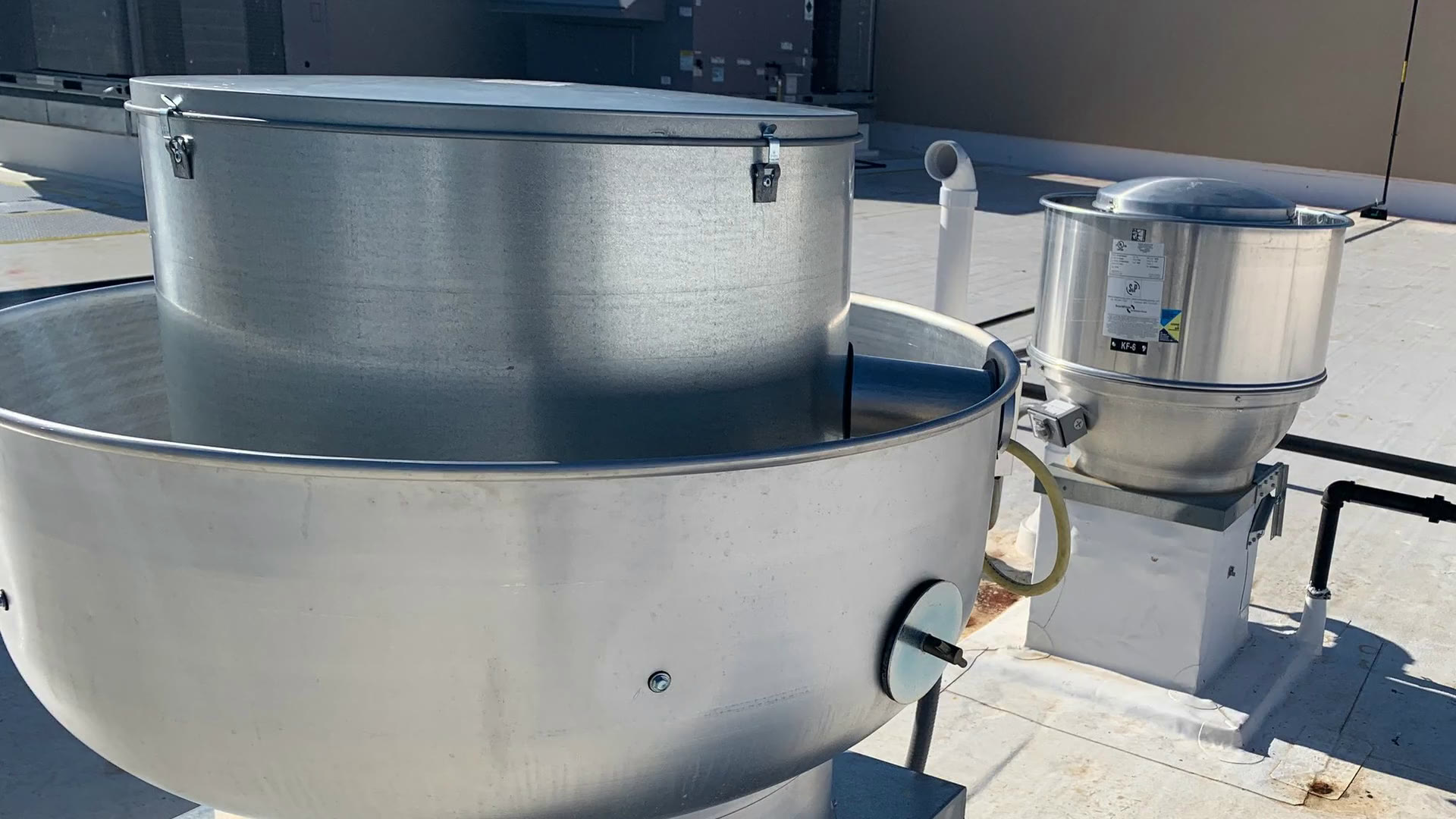 Two stainless steel kitchen exhaust fans on a restaurant rooftop under a deep blue sky
