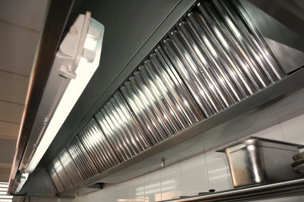 A commercial stainless steel kitchen hood with clean baffle filters, lit from inside