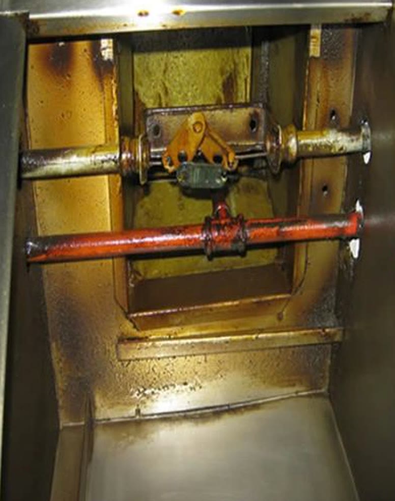 Inside a kitchen hood before cleaning, thick amber grease over the damper