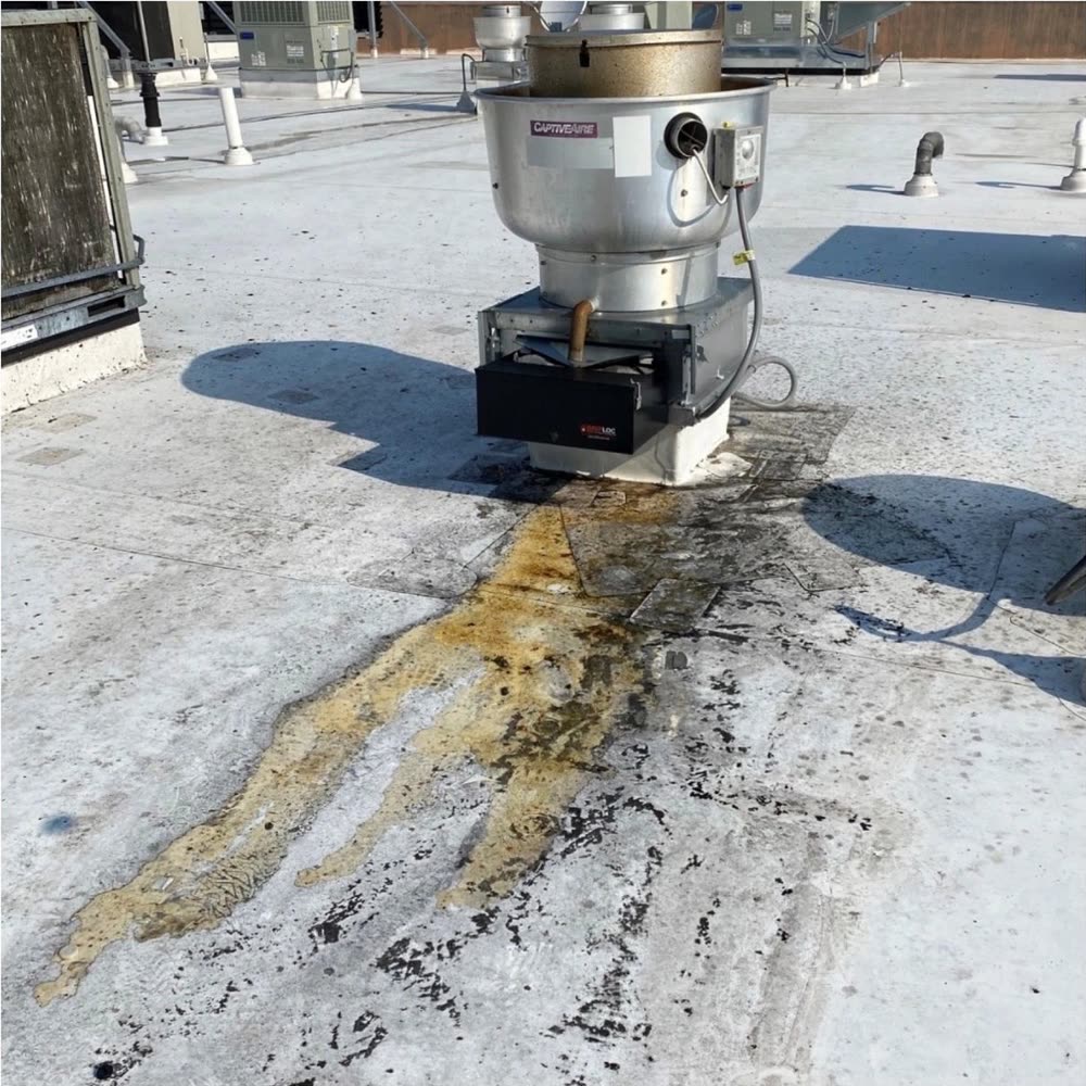 A rooftop exhaust fan with a long amber grease trail staining the white roof membrane