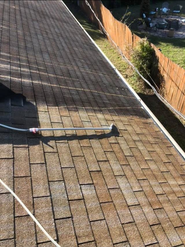 A soft wash lance cleaning an asphalt shingle roof, a clean stripe left behind