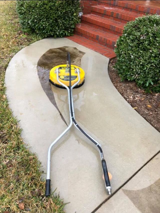 A rotary surface cleaner part way along a concrete path, clean concrete behind it